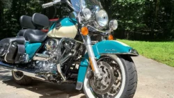 Blue and white motorcycle with chrome detailing, parked on a concrete surface with a grass and tree background.